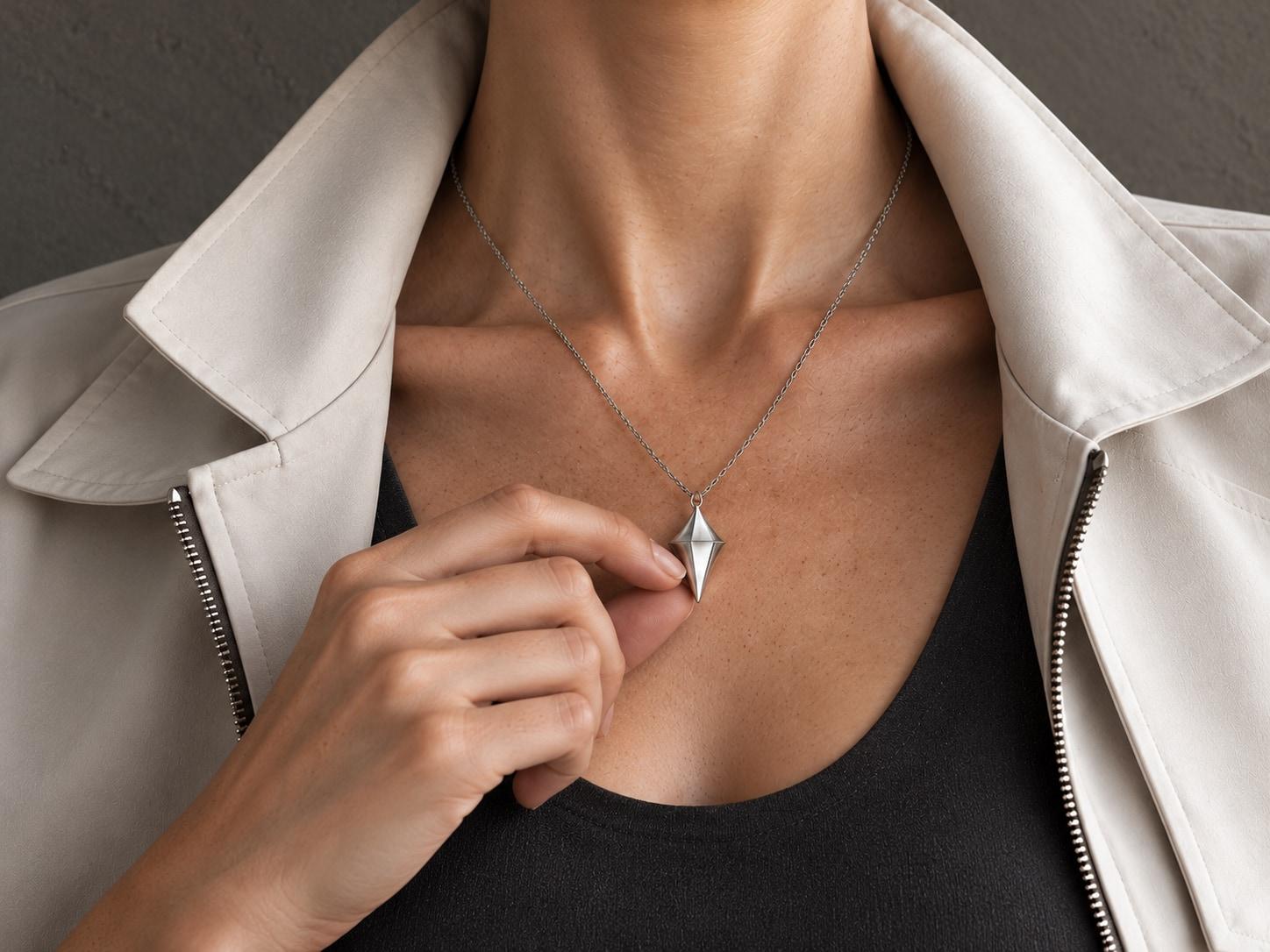 Close-up concept photograph of fingers gently turning the lower half of the silver pendant while it stays on its chain