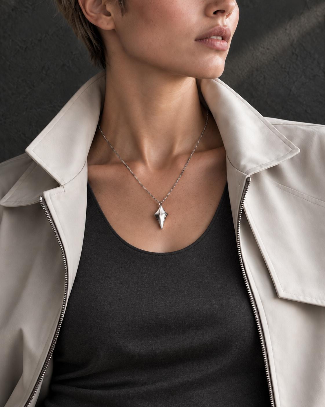 Concept photograph of the silver Glimmers pendant worn on a fine chain with charcoal crepe and a tailored stone jacket