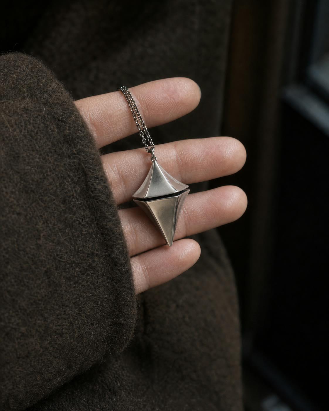Concept scale image of the geometry-correct titanium Glimmer pendant resting on fingertips